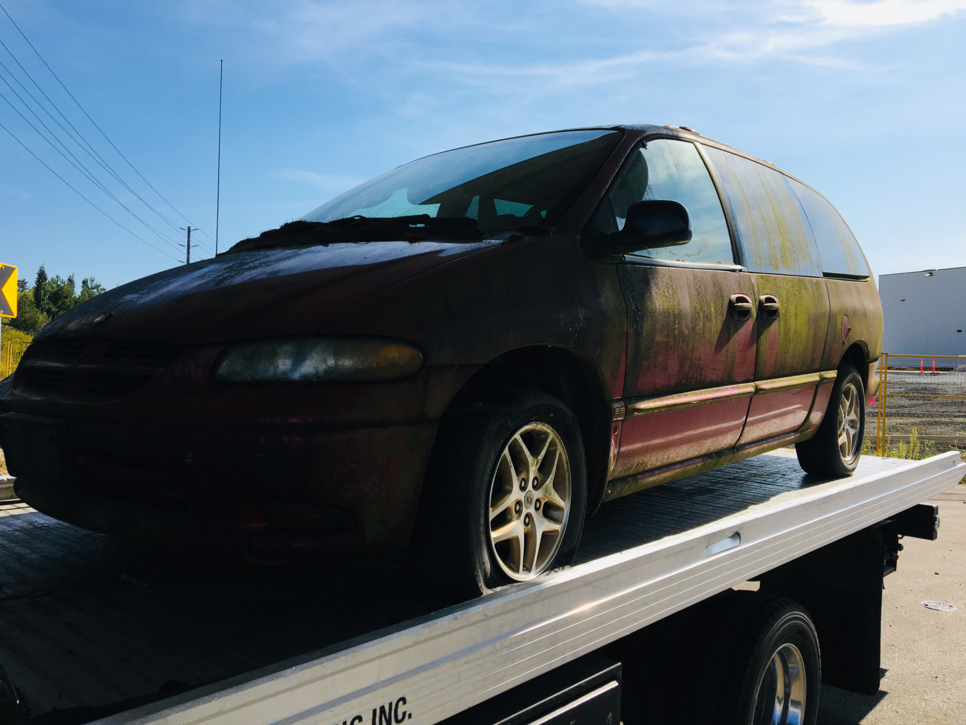 Red Dodge Grand Caravan covered in moss being towed away on a flat deck in Mission, BC